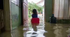 Mädchen sitzt im Hochwasser im Haus auf einem Stuhl