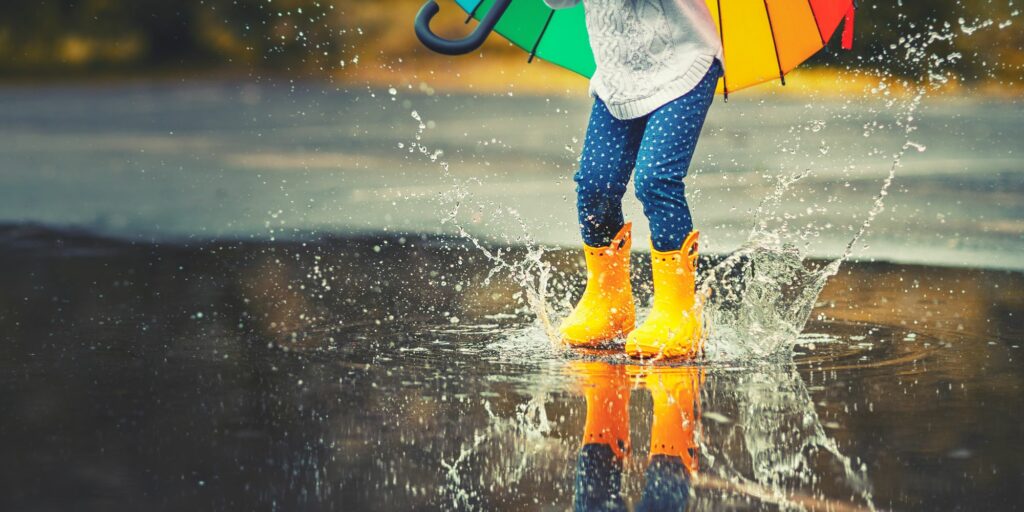 kind steht mit gummistiefeln im der regenpfütze